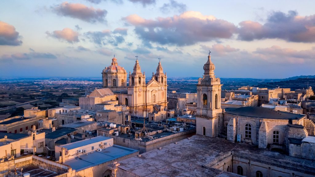 The city of Mdina, in Malta, is a top 10 destination for vacation in 2032 according to Sky Bird Travel & Tours travel blog. There is a large white church with old architecture in the center and medieval buildings surrounding it.