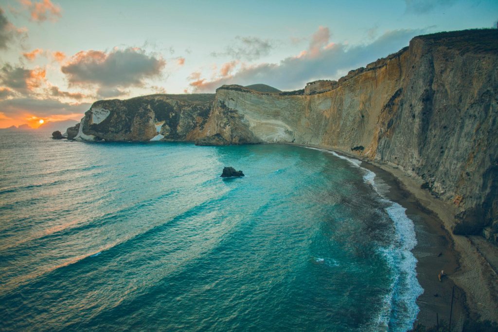A wide shot of the beautiful seaside ocean cliffs of exposed stone in Ponza, Italy. With the ocean waves crashing on the shore, it's the perfect summer vacation destination.