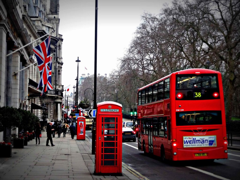 On the right of the picture sits a large red tour bus in the road, and a sidewalk with English flags and telephone booths on the other side. This is a bus tour, featured in Sky Bird Travel & Tours article about the different types of tours.