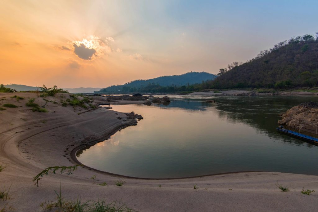 A soft orange sunset above a still lake called the Kampi dolphin pool, in the Mekong River. Kratie, Cambodia holds rare freshwater dolphins and can be seen on a customized tour with Sky Bird Travel & Tours.