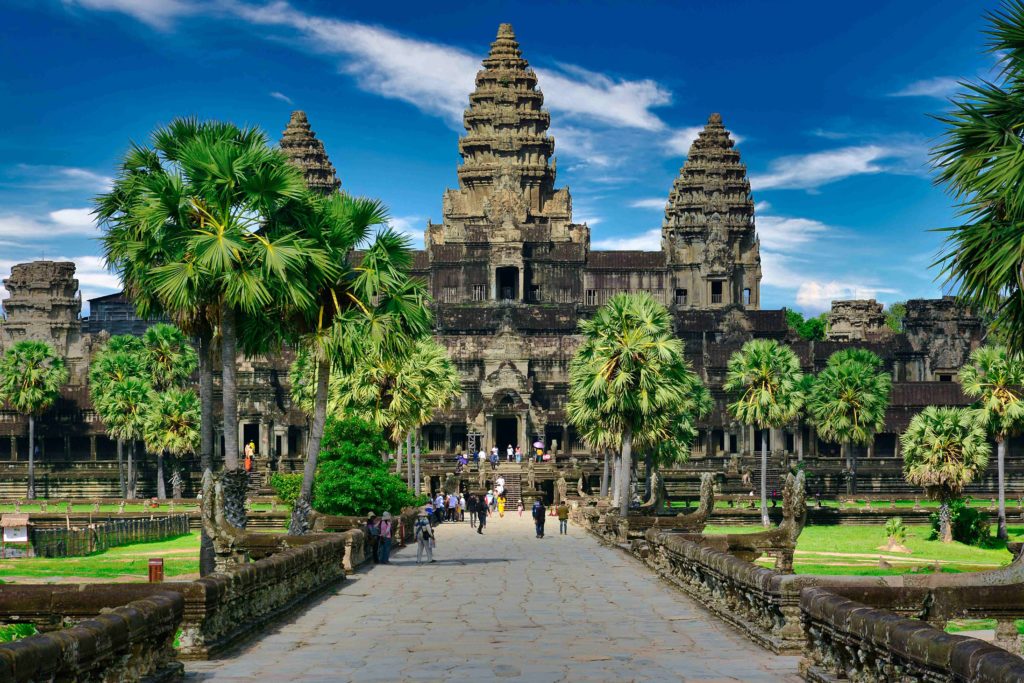 A beautiful travel photo of Angkor Wat Agkor in Cambodia, a large stone temple surrounded by palm trees. The front of the ancient temple represents important Cambodian history and can be toured with Sky Bird Travel & Tours.