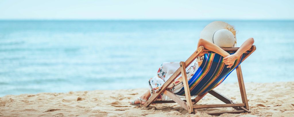 A fashionable woman reclines on a tanning chair at the beach looking into the blue sea on summer vacation. The featured image for Sky Bird Travel & Tours travel blog Top Summer Destinations for 2023."