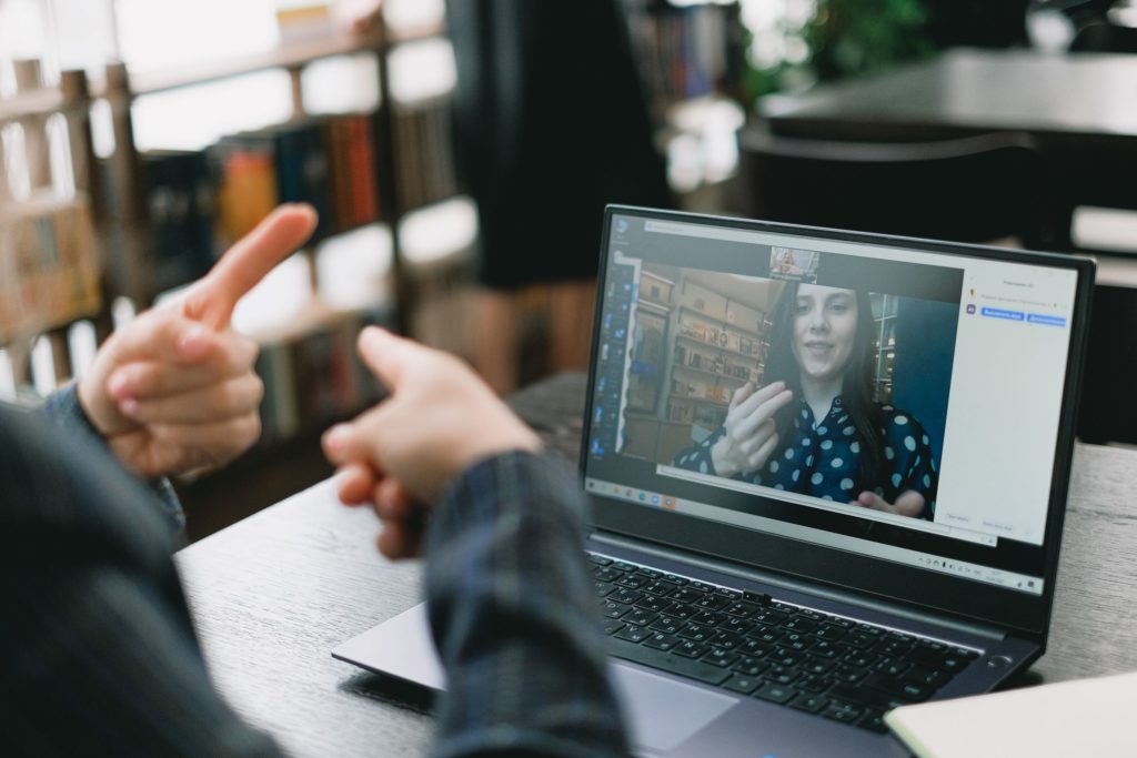 A female travel agent is using her computer to virtually meet online with her male client in a library to plan travel and tours, breaking the myth that airline consolidators are unreachable.