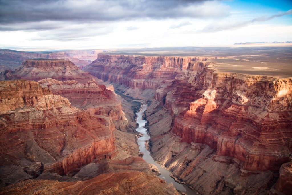 This photo was taken at the legendary Grand Canyon National Park in Arizona, United States near the Colorado River. A giant canyon made of red rocks sits in the foreground with the desolate Arizona desert in the background.