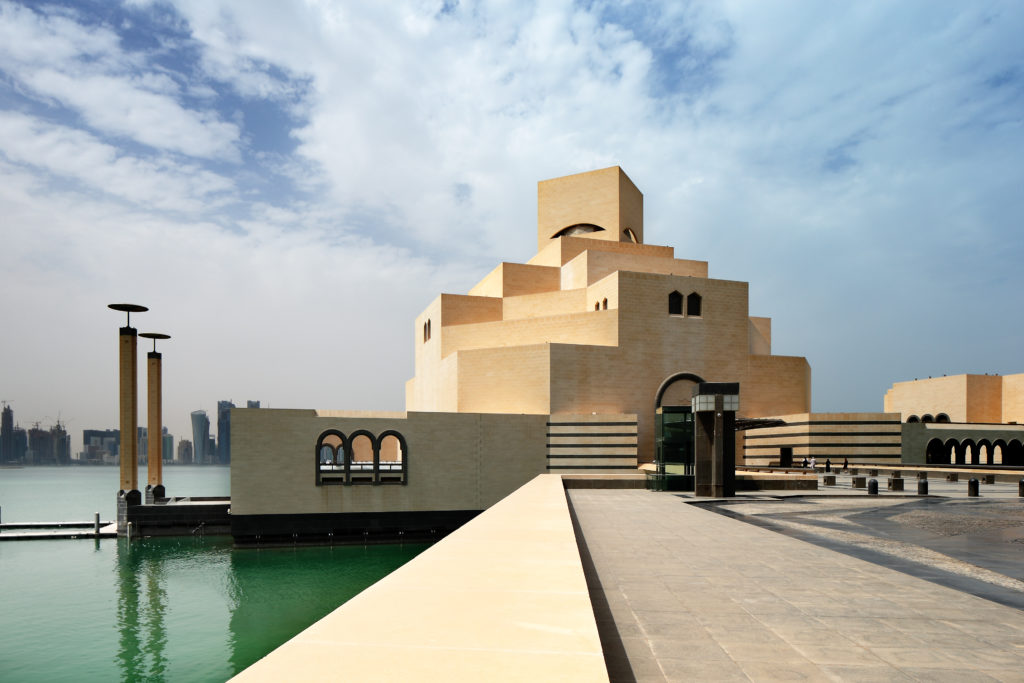 A sandstone building with modern architecture sits on the ocean and welcomes travelers looking to attend the Qatar Grand Prix 2023 formula 1. This is the Museum of Islamic art in Doha, Qatar, Middle East and can be toured with Sky Bird Travel & Tours.