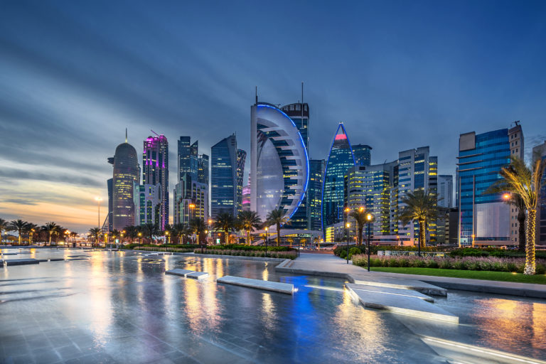 Sky Scrapers and modern buildings light up the night sky and reflect the luxury of Doha, Qatar in the Middle East. This image is the West Bay on the Corniche, and is used in Sky Bird Travel & Tours blog about the top destinations of 2023.