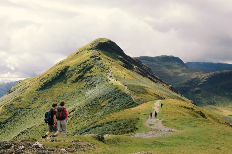 various groups of hikers are walking along a narrow trail to the top of a grassy mountain, exploring the best national parks to travel to in 2023 according to the Sky Bird Travel blog.