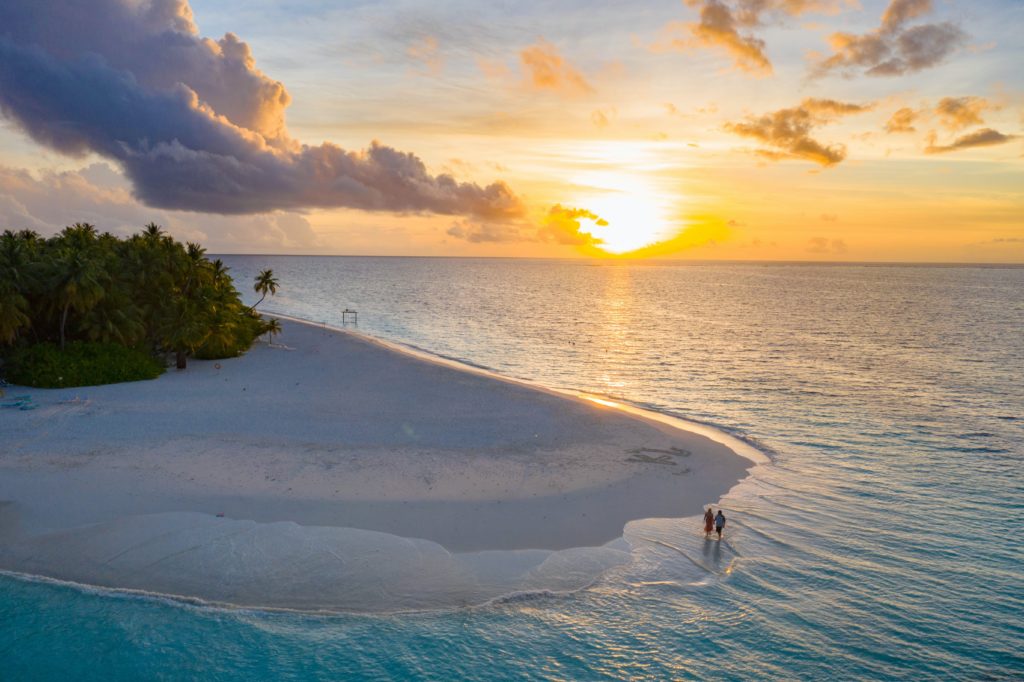 A landscape shot of St. Lucia at sunset, while a happy couple takes a romantic walk on the beach near the waves. This image is featured in the Sky Bird Travel & Tours blog, "Best Destinations for Honeymooners," which shows travel agents the most romantic locations for honeymoon!