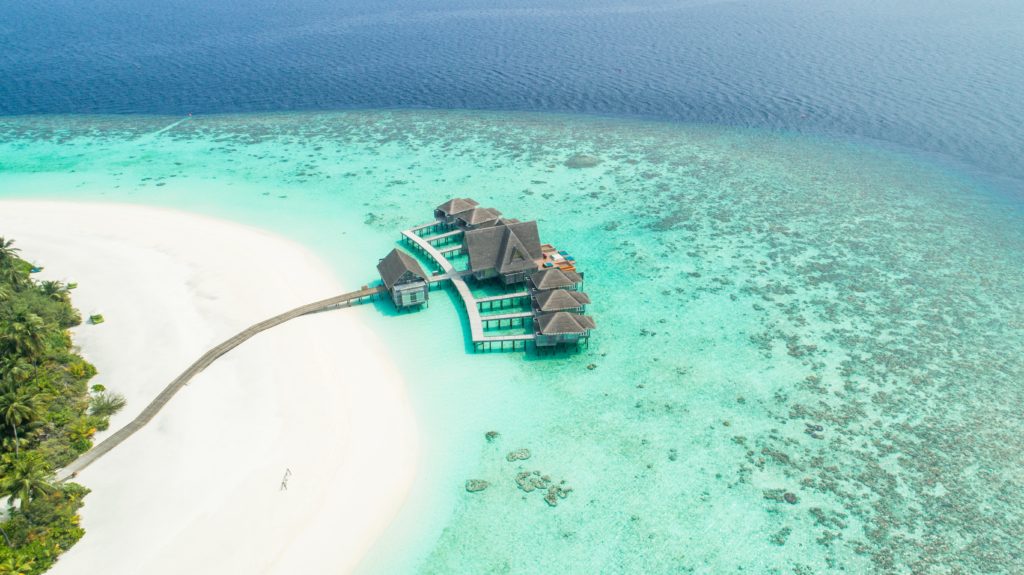 A landscape shot of the beautiful Maldives, with a small villa in the water and bright blue ocean as far as the eye can see. This image is featured in the Sky Bird Travel & Tours blog, "5 Spots To Send Clients Before it's Too Late," which describes the top locations that are being permanently destroyed.