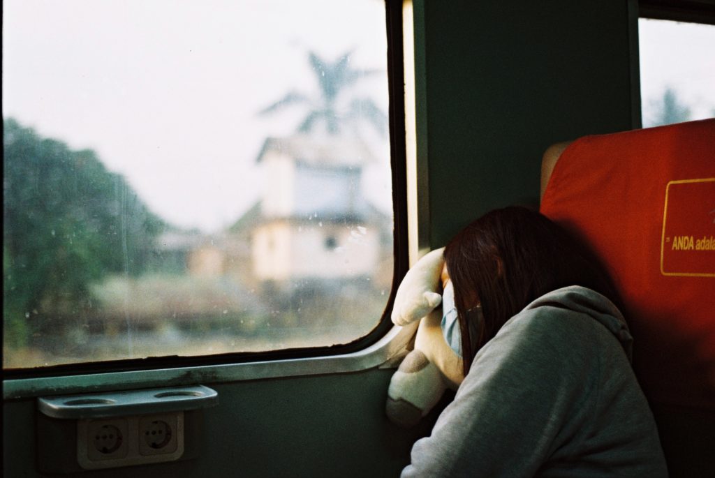 A woman lays with her head against the window of a moving train, taking a nap during her sustainable railway ride which cuts down on carbon emissions. This image is featured in the Sky Bird Travel & Tours blog, "Encourage Safe and Responsible Travel," which shows travel agents how to guide their clients on a safe vacation!