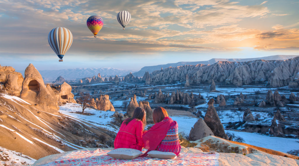 This Image of a couple watching people fly in a hot air balloon in Cappadocia is featured in the Sky Bird Travel & Tours tour blog, "Best Honeymoon Destinations," which lists the most romantic locations for newlyweds and couples.