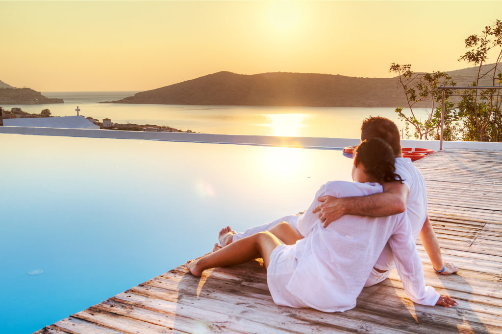 This Image of a couple sitting by a luxury pool watching the sunset is featured in the Sky Bird Travel & Tours tour blog, "Best Honeymoon Destinations," which lists the most romantic locations for newlyweds and couples.
