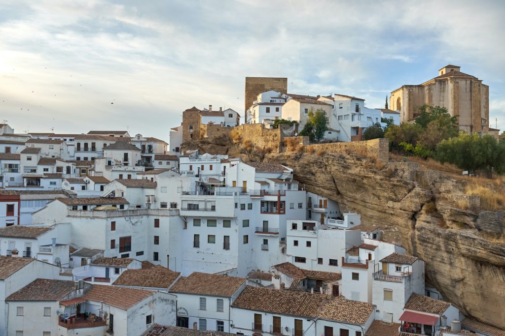 featured in Europe's Hidden Gems by Sky Bird Travel & Tours this image shows the town of setenil de las bodegas in Spain in Europe with whitewashed houses below a cliff.