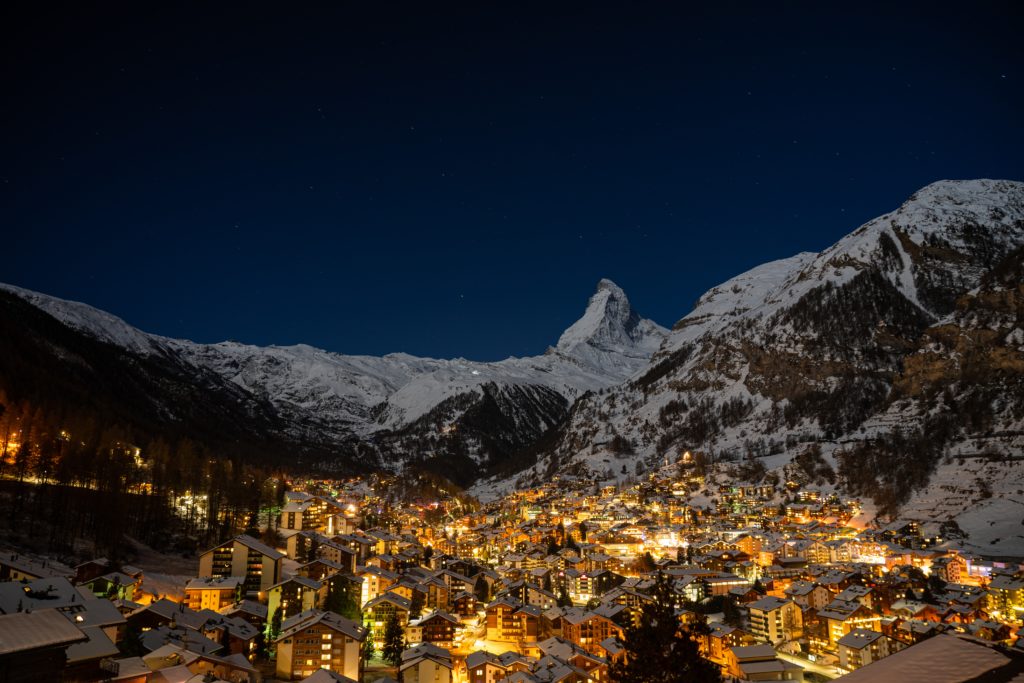 Featured in Europe's Hidden Gems by Sky Bird Travel, this image shows the town of Zermatt, Switzerland nestled between two mountains and lit up at night.