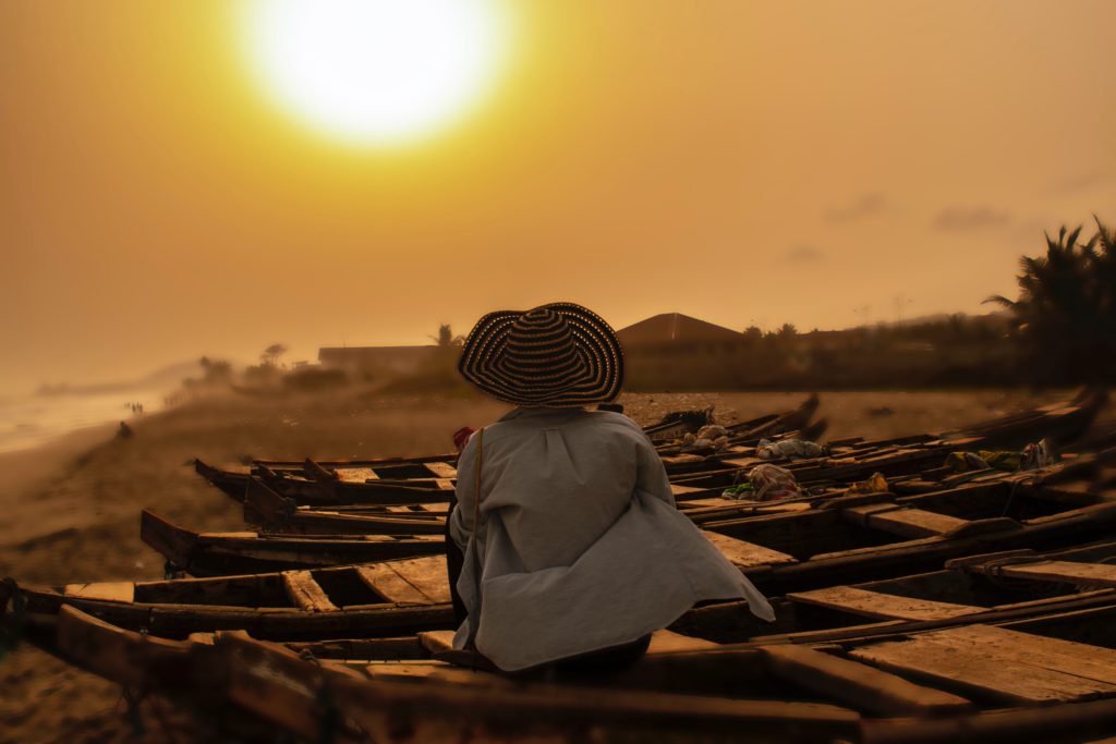 Featured in Top 10 Destination: Ghana by Sky Bird Travel & Tours, this image shows a woman sitting on a beach during sunset.