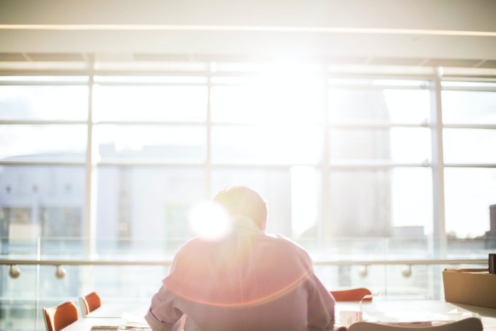 The featured image of "Why Travel Agents Need GDS" by Sky Bird Travel & Tours, this features the back of a mans head as he leans forward in front of a window of sunlight.