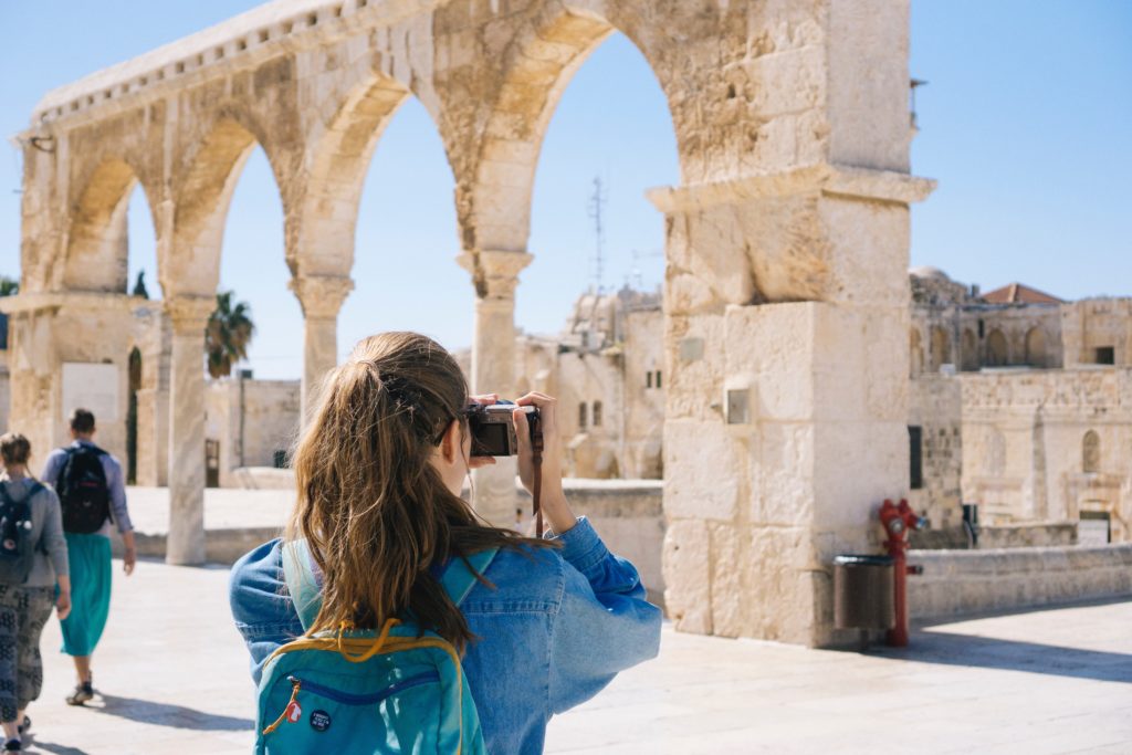 Featured in the blog "How To Celebrate World Tourism Day" by Sky Bird Travel & Tours, this image shows a female tourist in athens, greece taking a photo of ancient temple ruins.