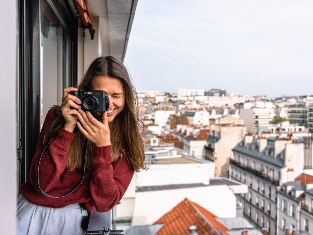 Featured in the blog "How To Celebrate World Tourism Day" by Sky Bird Travel & Tours, this image shows a female tourist leaning out of the hotel balcony to snap a photo.