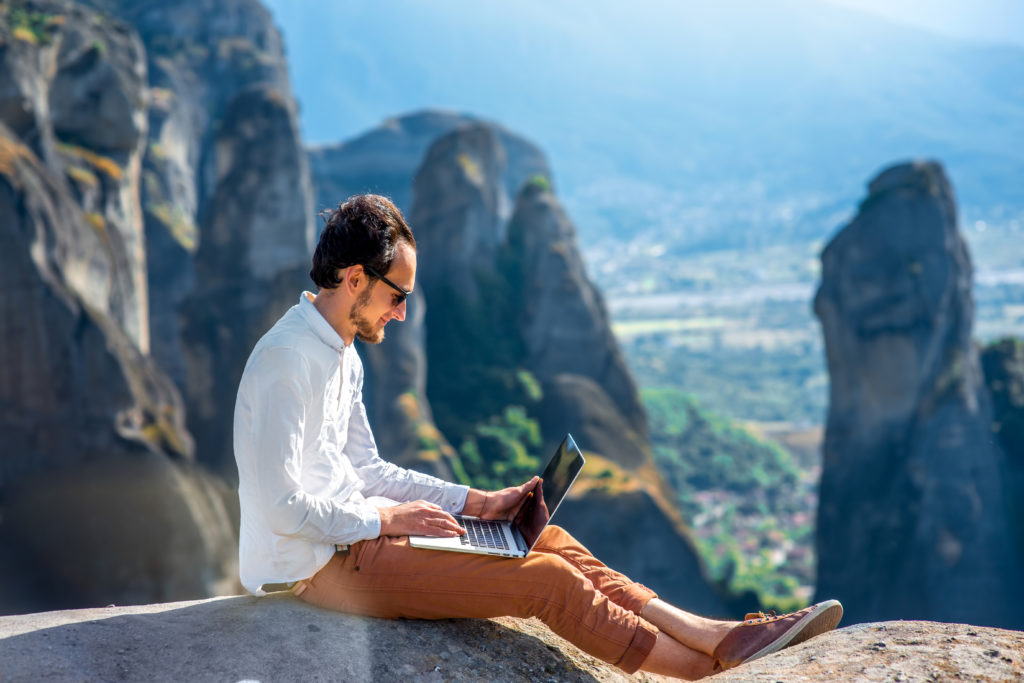 Featured in Discovering Niche Markets by Sky Bird Travel & Tours, this image shows a man sitting on a mountain typing on his laptop.