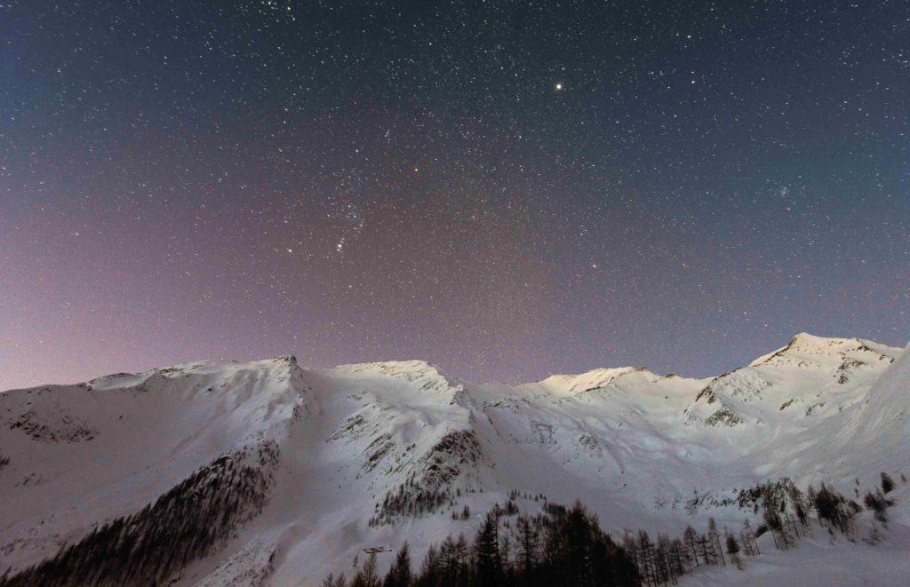 Featured in 2023 Winter Vacation Destinations from Sky Bird Travel & Tours, this image shows a starry night sky above a snowy mountain.