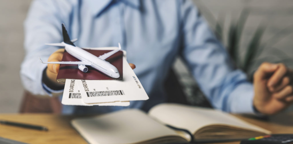 SKY BIRD WHY AGENTS SHOULD BOOK AIRFARES blog- Picture of travel agent with flight tickets and plane model in hand at agency office from Sky Bird Travel blog