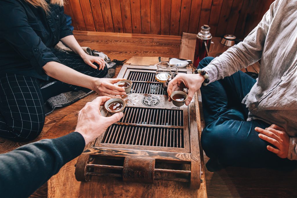 Featured in the blog Trending Travel Experiences of 2025 by Sky Bird Travel & Tours, this image shows a Group of people are sitting on the floor next to the tea ceremony table, friends are drinking tea and talking,table with ceramic white cups and glass teapot for Chinese tea ceremony.