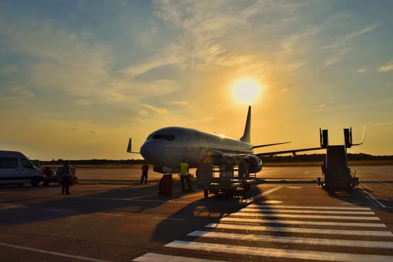 Sunset at the airport: a white passenger plane on the tarmac with ground crew loading luggage nearby.