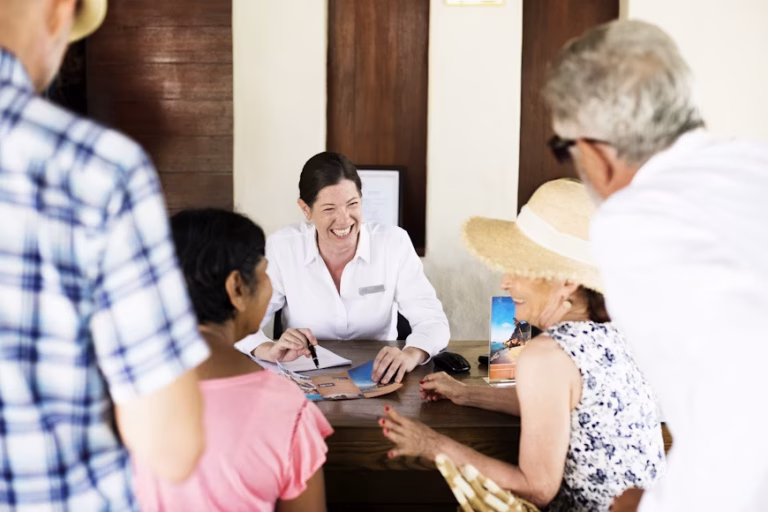 Travel agent in a white shirt helping a group of seniors with brochures at a desk.
