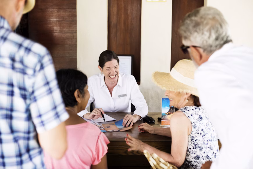 Travel agent in a white shirt helping a group of seniors with brochures at a desk.