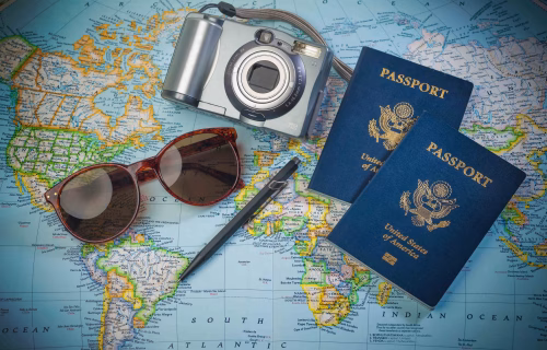 Camera, two blue US passports, and brown sunglasses laid on a world map for travel planning.