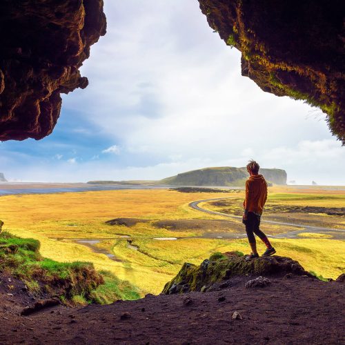 On a hiking expedition, purchased from Sky Bird Travel & Tours Sky Vacations, a woman climbs to the top of the Loftsalahellir Cave in Iceland and looks out over the green land and cliffs that attract tourists worldwide.